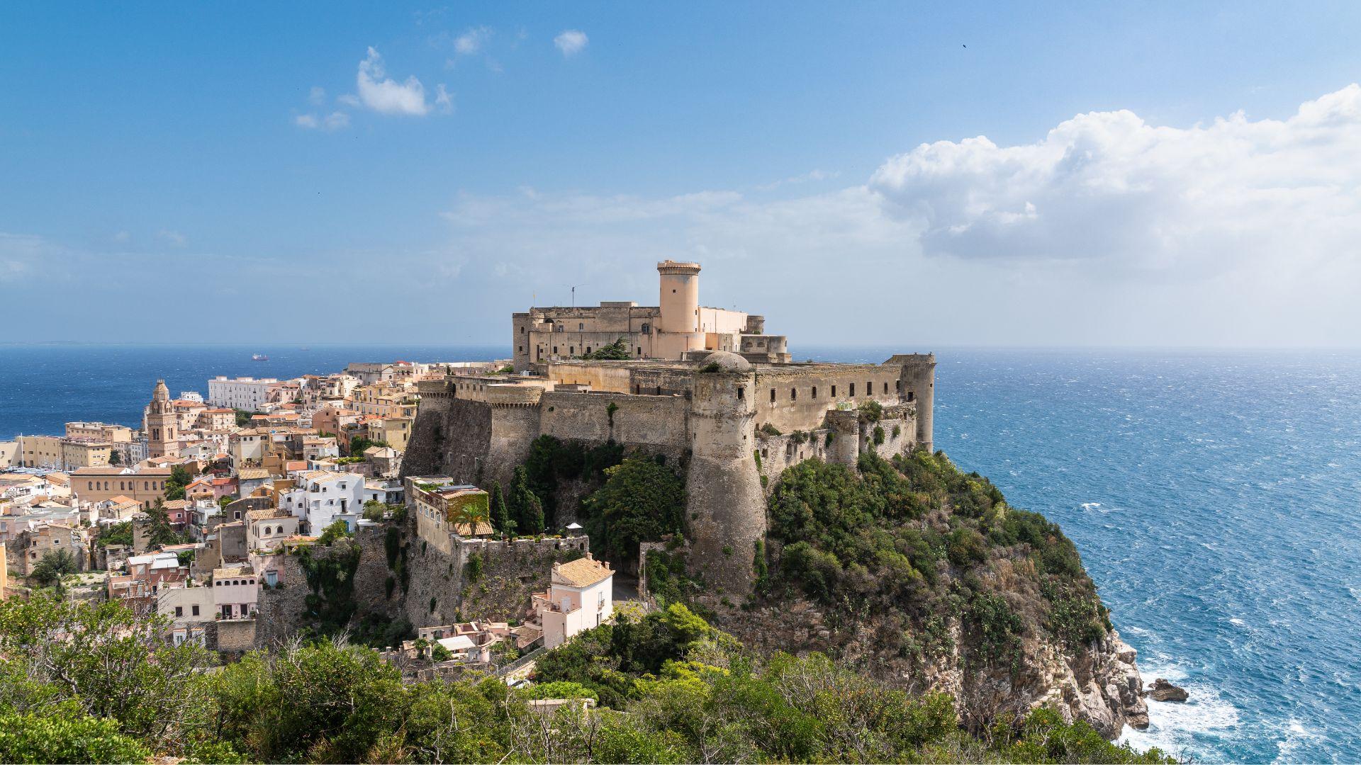 Castello medievale su una scogliera con vista sul mare e case colorate.