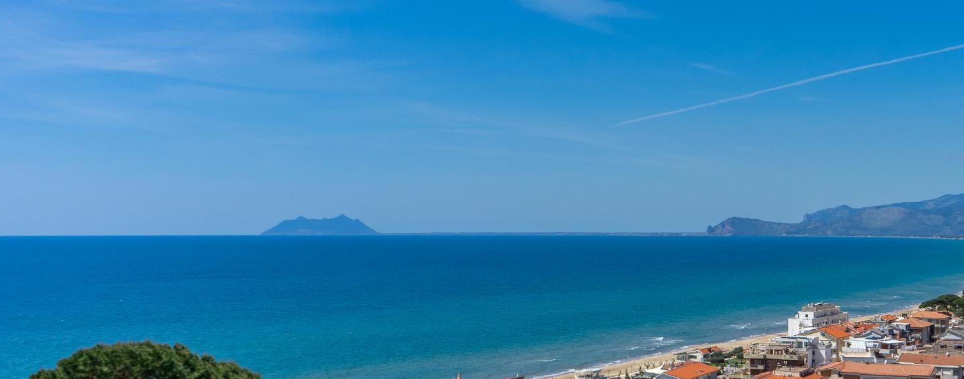 Vista panoramica sul mare con pini in primo piano e spiaggia in lontananza.