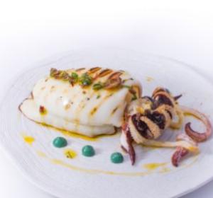 Calamaro grigliato con decorazione di salsa verde su piatto bianco elegante.