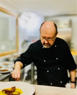 Chef in cucina mentre impiatta un piatto con cura e concentrazione.