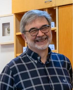 Uomo sorridente con barba e occhiali, indossa giacca e cravatta.