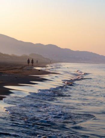 Spiaggia al tramonto con persone che camminano lungo la riva, onde leggere.