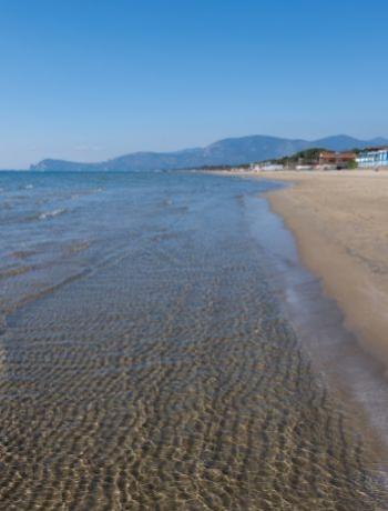 Spiaggia sabbiosa con mare calmo e montagne sullo sfondo in una giornata limpida.