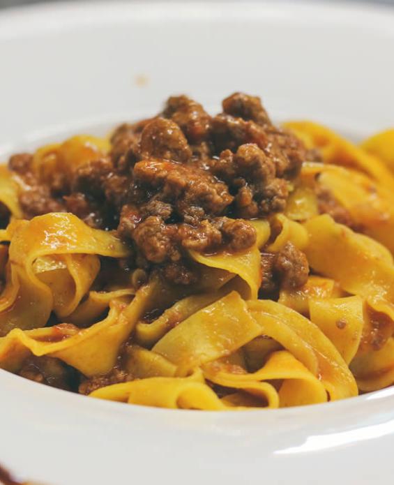 Tagliatelle al ragù di carne, servite su un piatto bianco con decorazione balsamica.