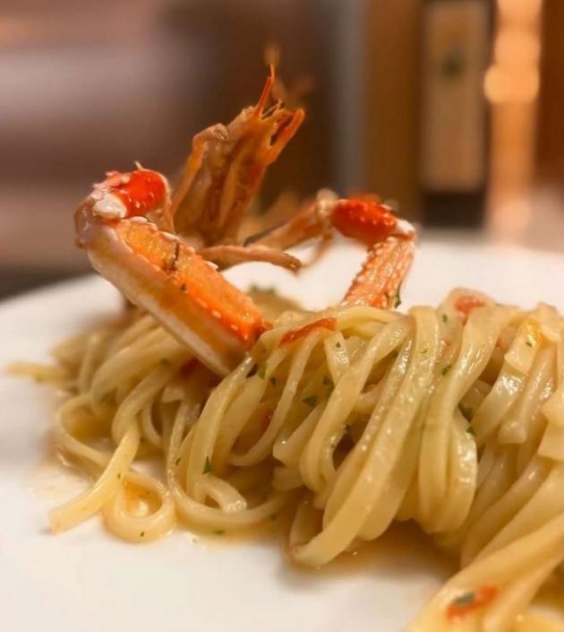 Spaghetti con granchio, decorati con prezzemolo e pomodoro, serviti su un piatto bianco.