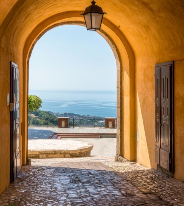 Arco con vista sul mare, pavimento in mattoni e lampione sospeso.