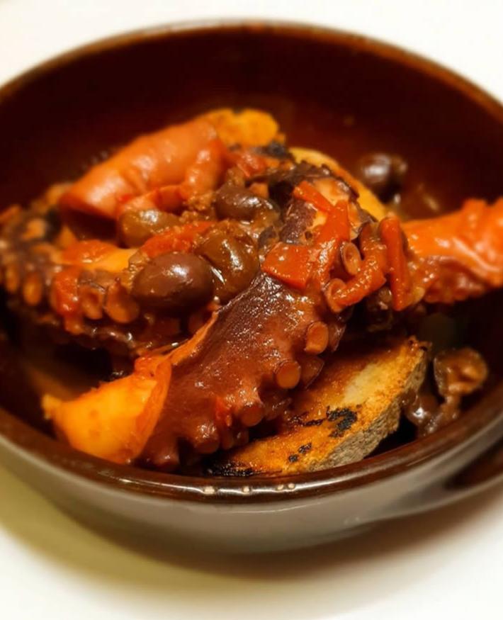 Polpo in umido con pomodoro e olive, servito su pane tostato.