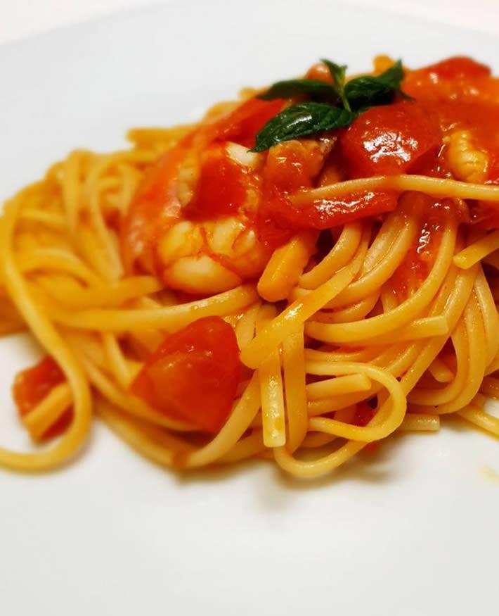 Linguine al pomodoro con gamberi, guarnite con foglie di basilico fresco.