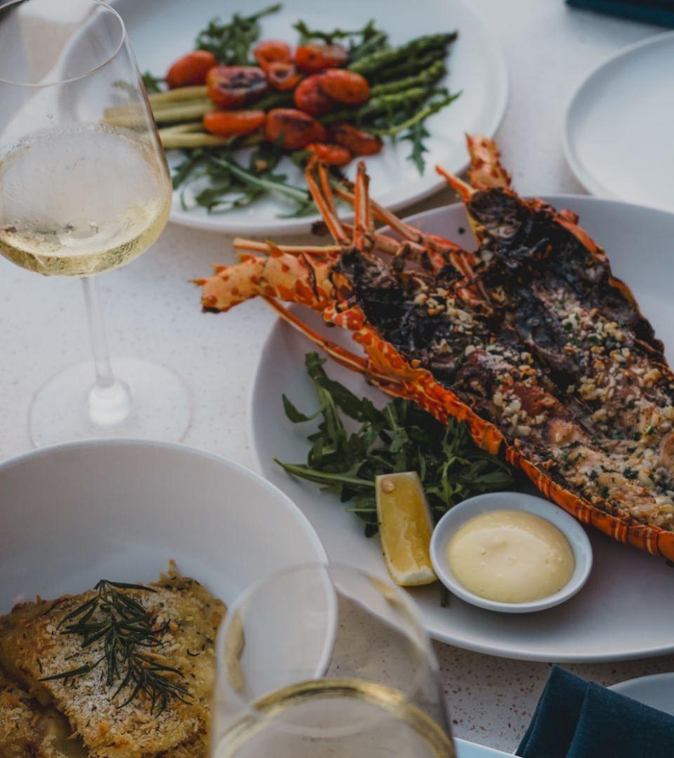 Cena elegante con aragosta, verdure grigliate e vino bianco.