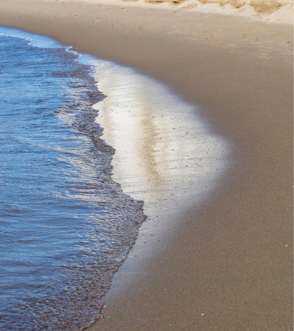 Spiaggia con onde che lambiscono la riva e riflessi di luce sull'acqua.