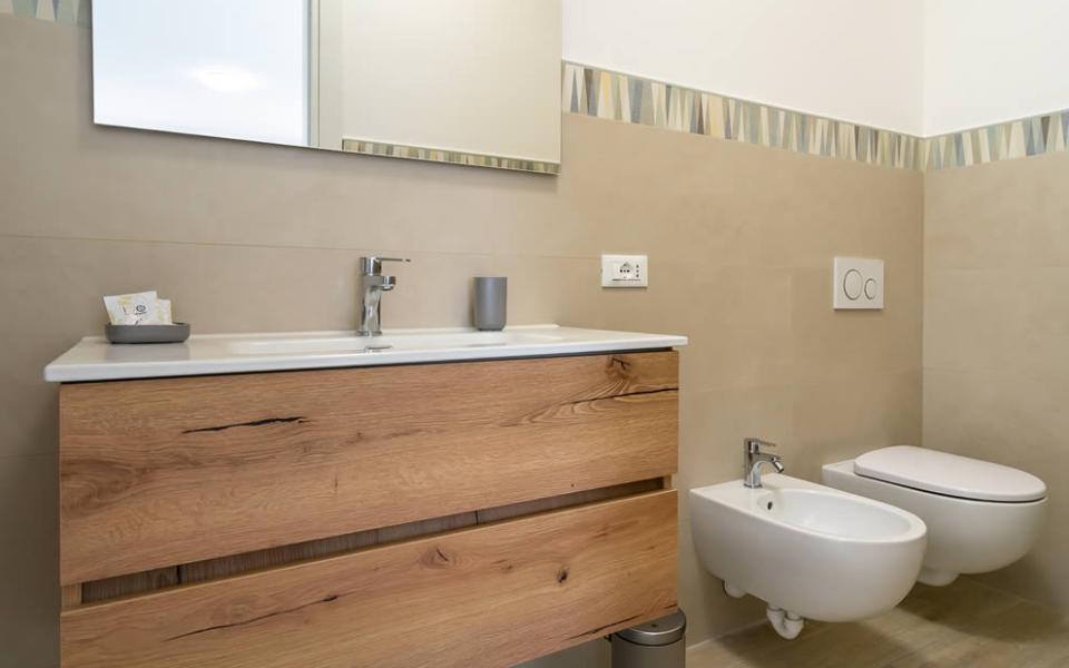 Elegante bagno moderno con lavabo in legno e sanitari sospesi, atmosfera accogliente e pulita.
