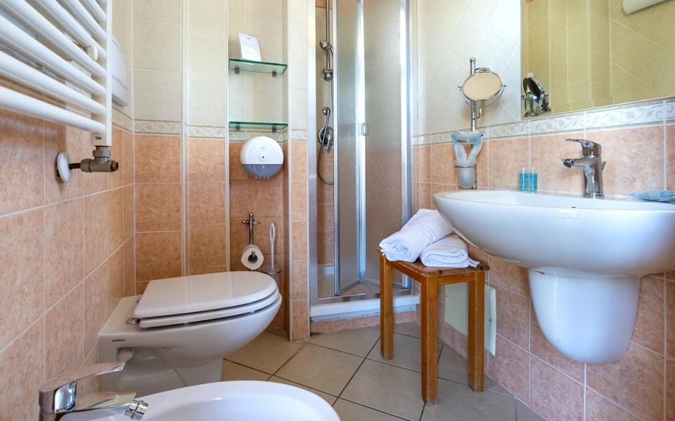 Bagno accogliente con doccia, colori caldi e asciugamani bianchi su sgabello.