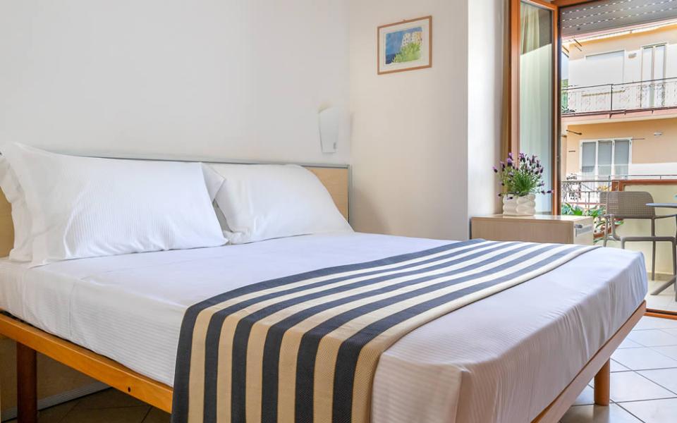 Camera da letto con copriletto a righe, accappatoi e fiori sul comodino.