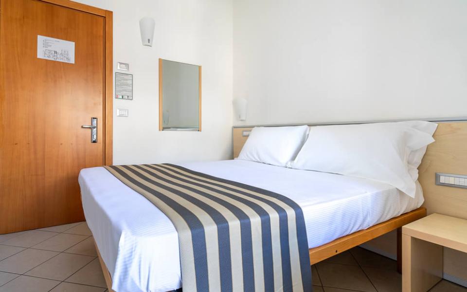 Camera da letto con letto matrimoniale, copriletto a righe e fiori sul comodino.