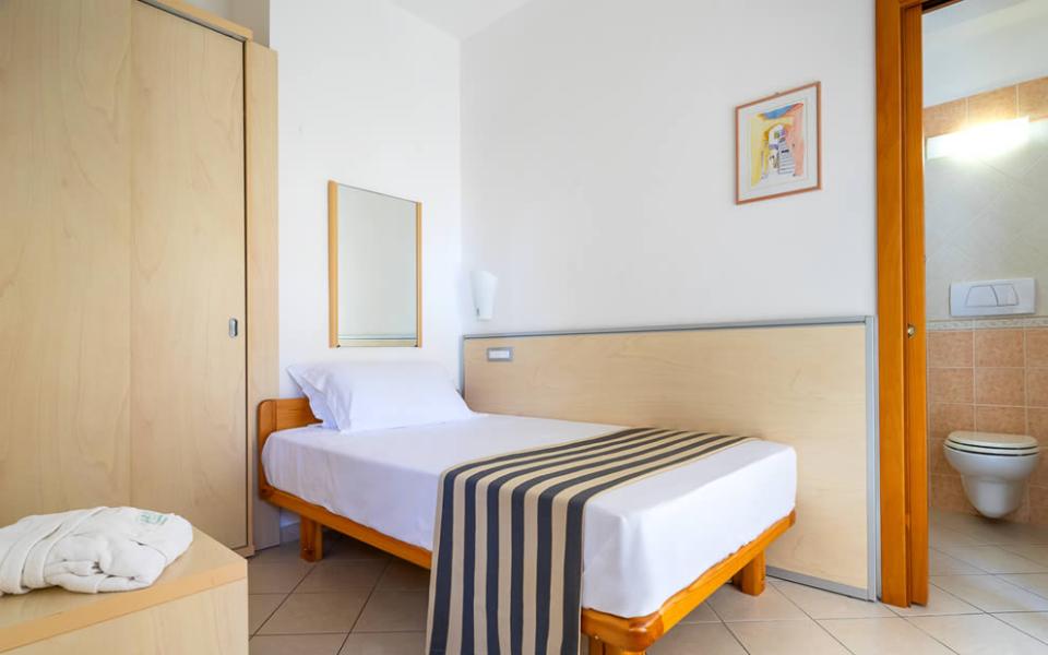Letto con petali di rosa, bottiglia di vino e calici sullo sfondo.