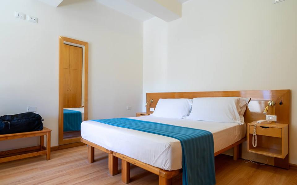 Camera luminosa, letto accogliente, dettagli in legno, atmosfera calda e rilassante.